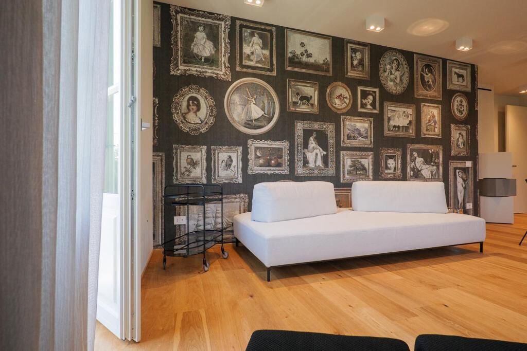 Una stanza con un divano bianco, un muro decorato con quadri incorniciati e un carrello nero.
