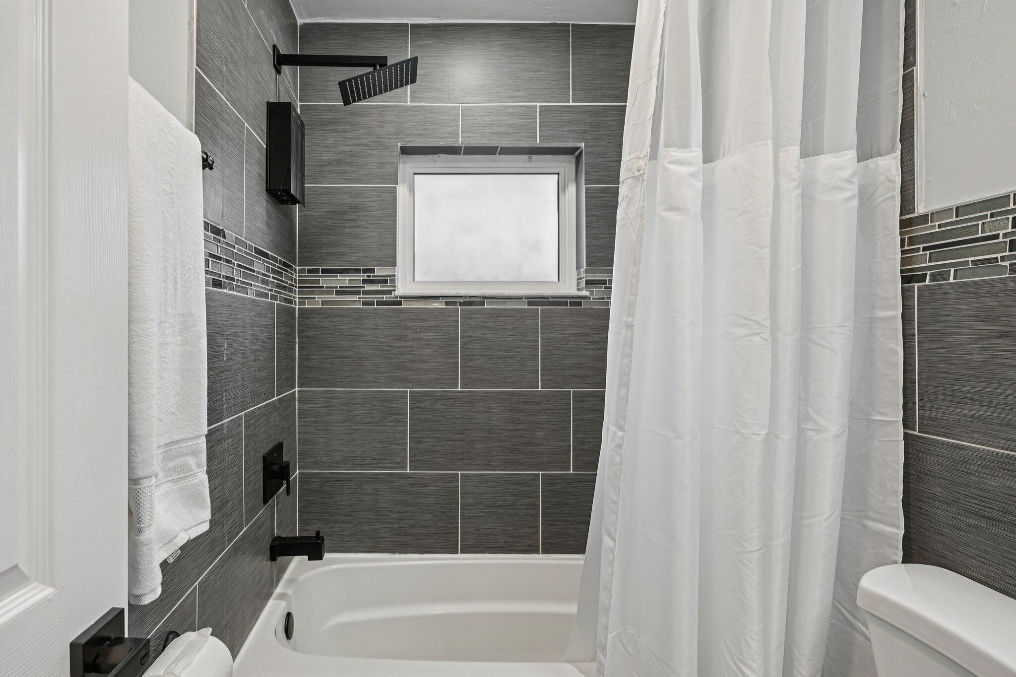 Een moderne badkamer met een bad, een raam en een douchegordijn.