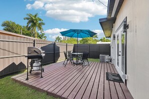 A deck with a grill, outdoor table and chairs, a blue umbrella, and a 'hello' mat. - 2BD-2BA Retreat -Fast Wi-Fi- Near Beach & Downtown (North Fort Myers)