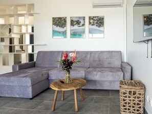 A modern living room with a grey sofa, a wooden coffee table with a vase of flowers, and a wicker basket. - 972L2 - T4 "Kalinago" facing the sea (Le Vauclin)