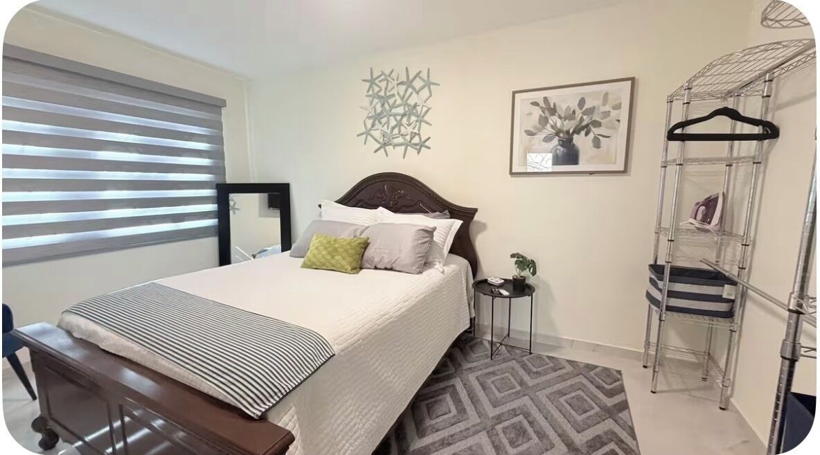 A bedroom with a bed, bedside table, lamp, and a metal storage unit.
