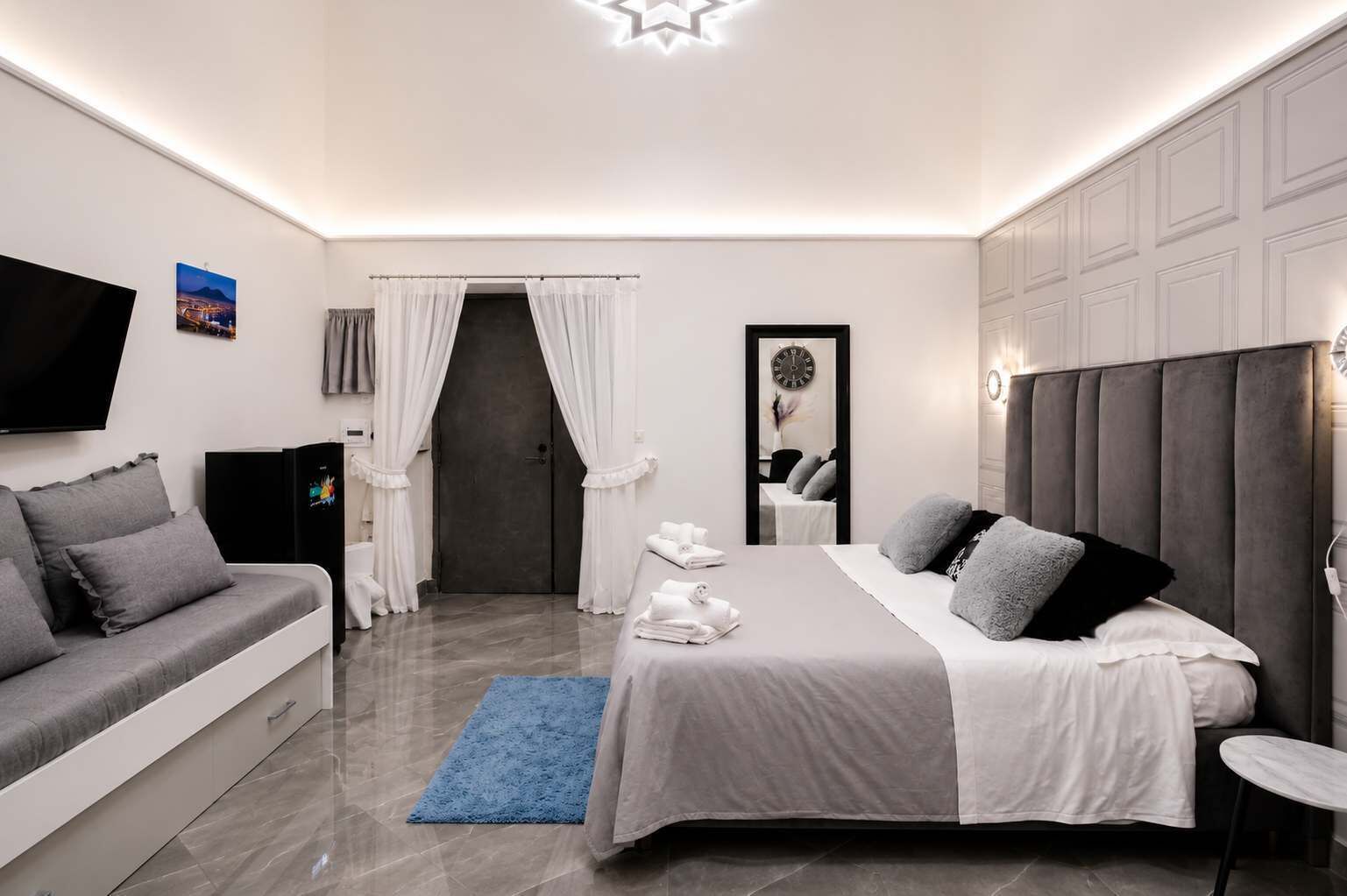 Habitación de hotel moderna con cama, sofá, televisión y baño visible a través de una puerta.