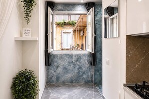 A hallway with a view into a room with a window, a marble wall, and a plant. - La Casetta di Gelsomina | Centro Storico | 4 pax (Napoli)