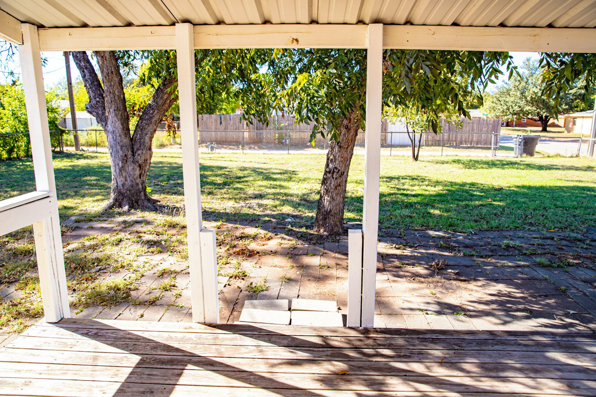 A covered outdoor area with a wooden deck, trees, and a grassy yard.