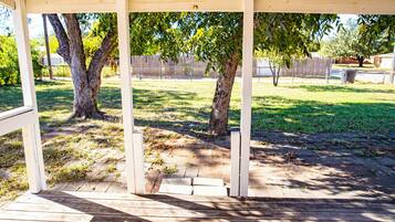 A covered outdoor area with a wooden deck, trees, and a grassy yard.