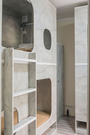 Una cama individual en literas con ventilador incorporado, un espacio reducido cerrado y un baño con ducha.
