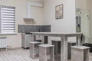 Una cocina moderna con encimera de mármol, armarios blancos y un amplio ventanal con persianas.