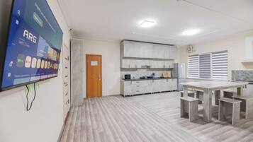 Una habitación amplia con una gran televisión de pantalla plana montada en la pared, una puerta de madera, una zona de cocina con encimera de mármol y una mesa de comedor con bancos.