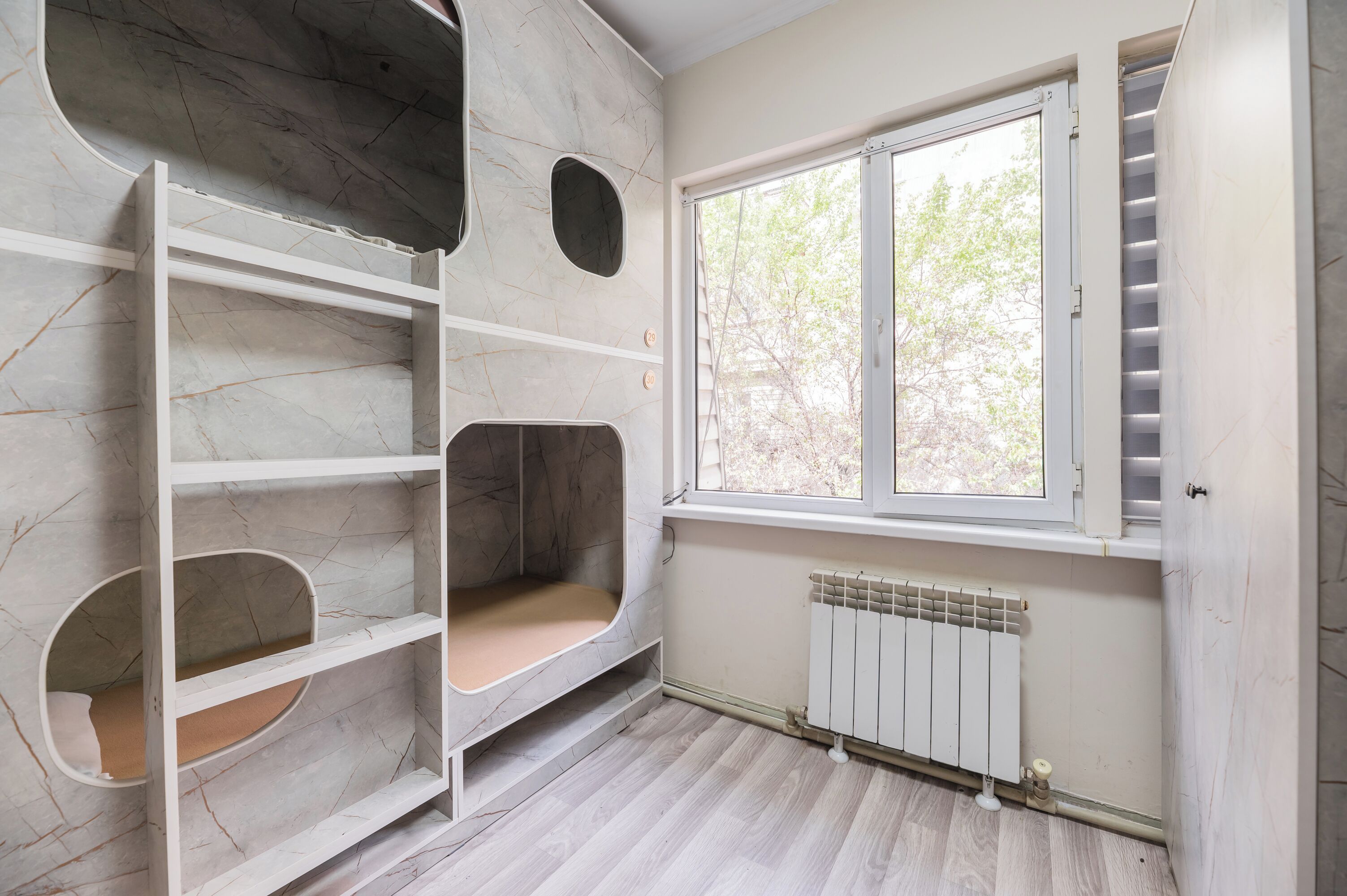 A room with a built-in shelving unit, a window with a view of trees, and a radiator.
