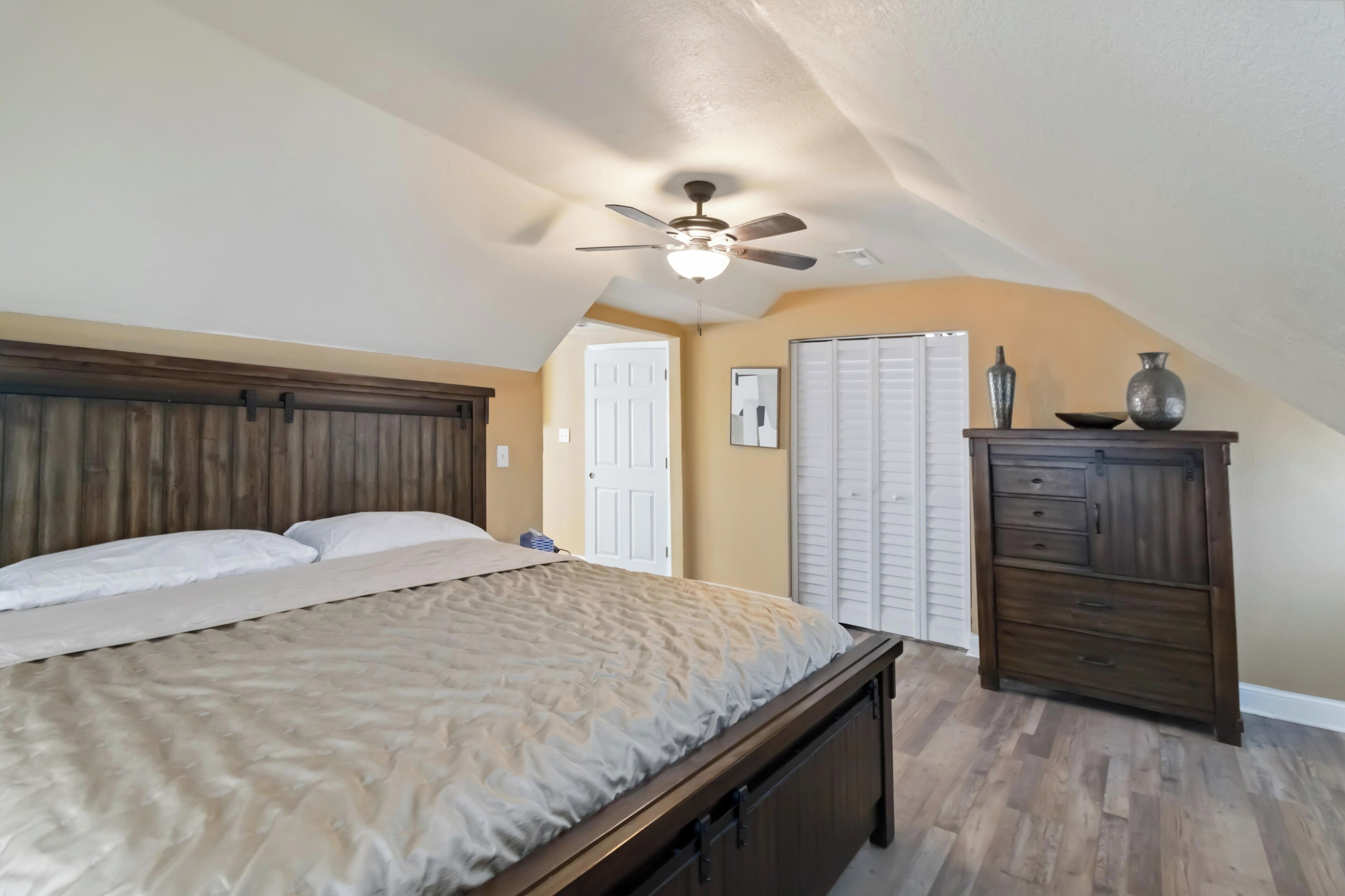 A bedroom with a bed, a ceiling fan, a dresser, and a door.
