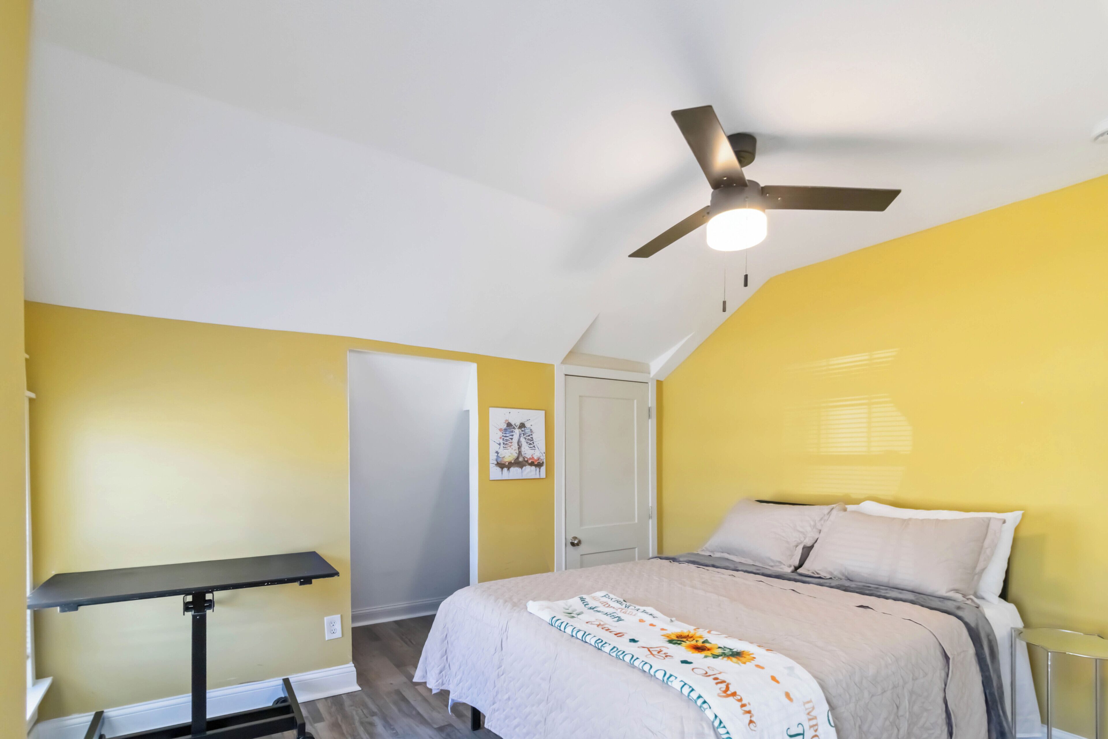 Ein Schlafzimmer mit Bett, Deckenventilator, Tür und einem kleinen Tisch.
