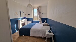 Ein Schlafzimmer mit Bett, Nachttisch, Lampe, Fenster mit Vorhängen und einem Spiegel an der Wand.