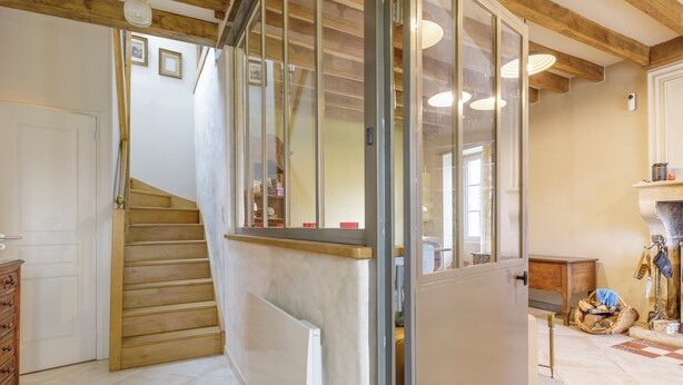 Una escalera que sube a un segundo piso, suelo de madera, una puerta blanca y una chimenea con una cesta y herramientas.