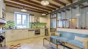 Una cocina con un salpicadero a cuadros, una zona de comedor con mesa de vidrio y un sofá con cojines estampados.