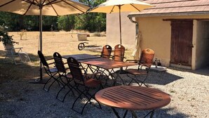 Un patio al aire libre con una mesa, sillas, dos sombrillas y un edificio al fondo.