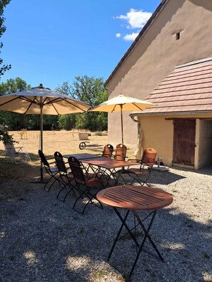 Une terrasse extérieure avec une table et des chaises, deux parasols et un bâtiment en arrière-plan.