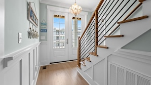 A hallway with a wooden staircase, white walls, and a chandelier. - Into The Mistic, Ocean Isle Beach (Ocean Isle Beach)
