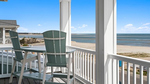 A porch with two green Adirondack chairs, a white railing, and a view of the beach and ocean. - Into The Mistic, Ocean Isle Beach (Ocean Isle Beach)