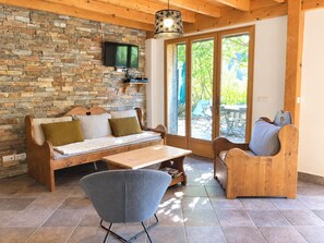 A cozy living room with a stone wall, wooden furniture, a flat-screen TV, and a sliding glass door leading to an outdoor area. - GITES LE MOULIN - LA COMPOTE (LA COMPOTE)