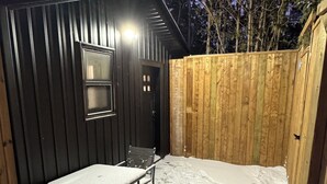 Un portico esterno coperto con tavolo e sedie, circondato da una recinzione di legno e un edificio in metallo.