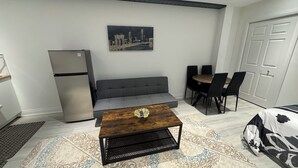 Un ambiente compatto con divano, tavolo da pranzo, sedie, tavolino, frigorifero e un dipinto con vista sulla città.