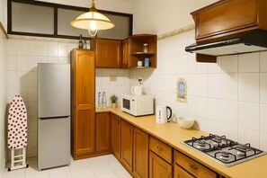 A kitchen with wooden cabinets, a gas stove, a microwave, a refrigerator, and a hanging lamp.