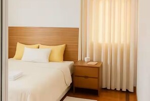 A hotel room with a bed, a nightstand, a lamp, and a window with curtains.