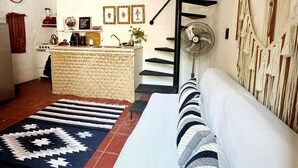 Un salon confortable avec un canapé, un tapis à motifs, un escalier et un coin cuisine équipé d’une cuisinière et d’un évier.