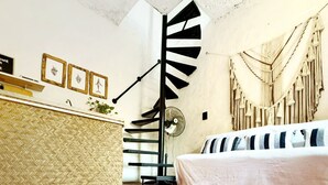 Une pièce dotée d’un escalier en colimaçon, d’un lit avec une literie à rayures, d’un tapis tissé et de décorations murales en macramé.