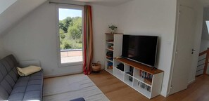 A living room with a sofa, a TV on a stand, a bookshelf, and a window with curtains. - Peace and quiet in the Pays d'Oust and Brocéliande regions (Montertelot)