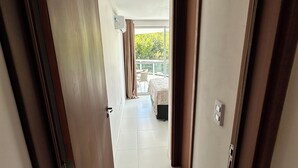 A hotel corridor with a view to a balcony, a bed, and a chair.
