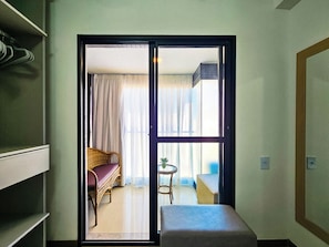 Quarto com porta de correr para uma varanda, uma cadeira de vime, uma mesa redonda pequena e um sofá.