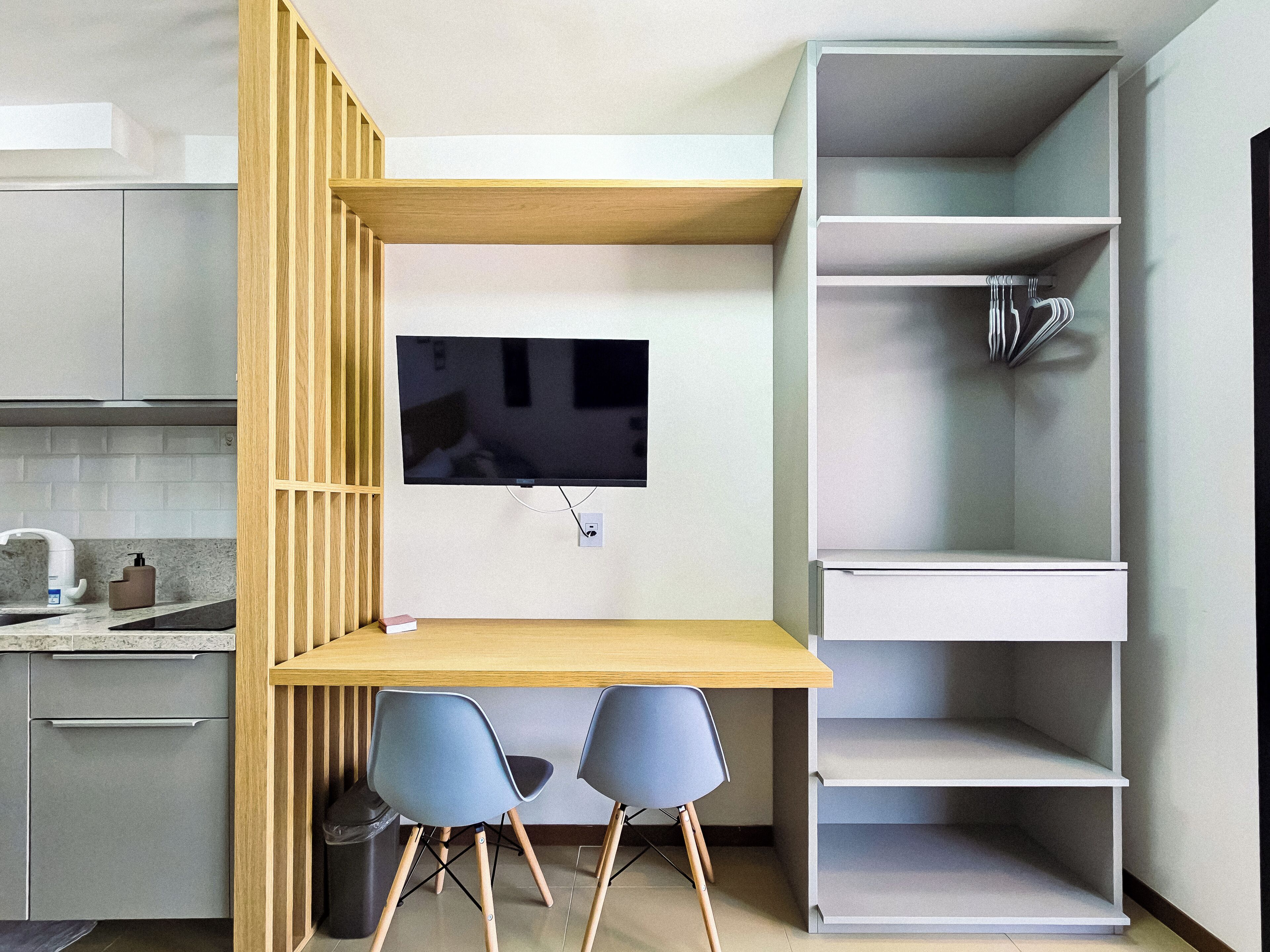 A compact kitchen with a built-in TV, a small dining area with two chairs, and a white shelving unit.