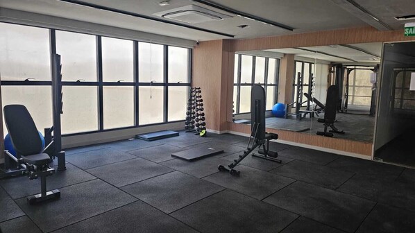 A gym with exercise equipment, large windows, and a mirrored wall. - Estúdio Vista Mar na Pituba (Salvador)