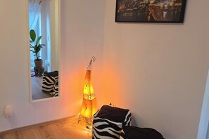 A room with a mirror reflecting a plant and a zebra-patterned pillow, a hanging lamp, and a framed picture on the wall.