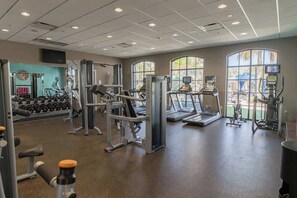 Ein Fitnessstudio mit unterschiedlichen Trainingsgeräten, großen Fenstern und einer Wanduhr.