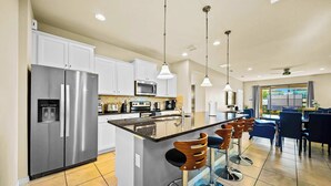 A modern kitchen with a central island, bar stools, stainless steel appliances, and pendant lighting. - Resort Home, Private Pool and Spa, Outdoor Theater (Kissimmee)