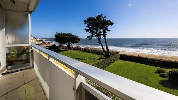 A balcony with a view of the ocean, a tree, and a grassy area. - Le sable au pied de la résidence T2 de qualité (Larmor-Plage)
