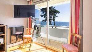 A room with a large sliding glass door leading to a balcony with a view of the sea. - Le sable au pied de la résidence T2 de qualité (Larmor-Plage)