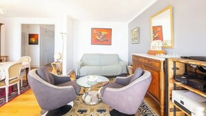 A living room with a sofa, two armchairs, a coffee table, a TV stand, and artwork on the walls. - Le sable au pied de la résidence T2 de qualité (Larmor-Plage)