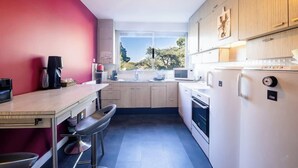 A modern kitchen with a dining area, a large window, and a view of the outdoors. - Le sable au pied de la résidence T2 de qualité (Larmor-Plage)