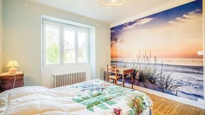 A bedroom with a large bed, a window, a radiator, a desk, and a beach mural on the wall. - Spacieuse résidence de famille cadre privilégié (Loctudy)