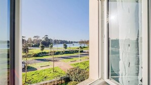 A view from a window overlooking a park with a lake, a road, and trees. - Spacieuse résidence de famille cadre privilégié (Loctudy)
