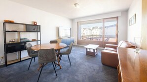 A modern living room with a round table, grey chairs, a sofa, a TV, and a bookshelf. - Plages & bourg à pieds : appartement 2 chambres (Larmor-Plage)