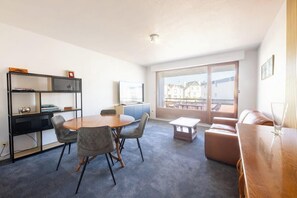A modern living room with a round table, grey chairs, a sofa, a TV, and a bookshelf. - Plages & bourg à pieds : appartement 2 chambres (Larmor-Plage)
