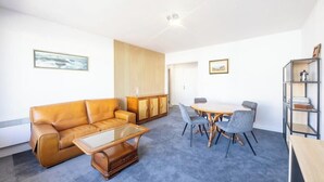 A modern living room with a leather sofa, a glass coffee table, a dining table with chairs, and a bookshelf. - Plages & bourg à pieds : appartement 2 chambres (Larmor-Plage)