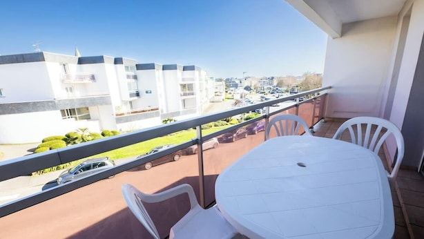 A balcony with a white table and chairs, overlooking a parking area and buildings. - Plages & bourg à pieds : appartement 2 chambres (Larmor-Plage)