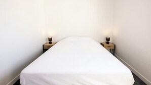 A narrow hotel room with a single bed, two bedside tables, and two wall-mounted lamps. - Plages & bourg à pieds : appartement 2 chambres (Larmor-Plage)