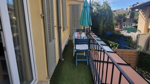 Een balkon met kunstgras, een tafel met stoelen en een groene parasol.