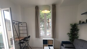 Een moderne woonkamer met een bank, een salontafel, een blauwe voetenbankje, een ladder en een raam met gordijnen.